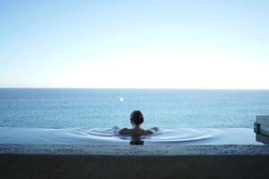 Person entspannt in einem Infinity-Pool mit Meerblick, Symbolbild fuer Nervensystem-Beruhigung und Sympathikus-Deaktivierung